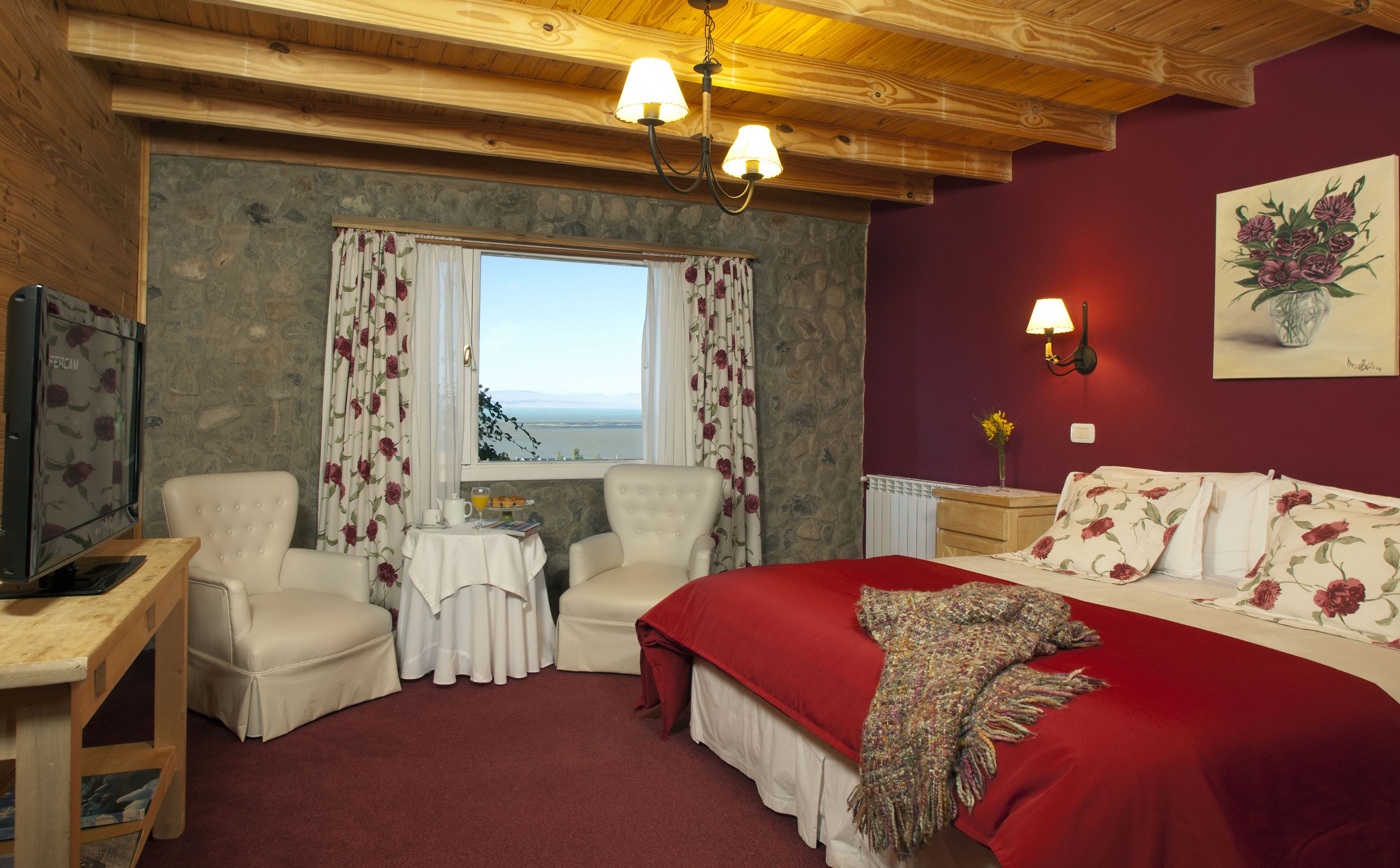 A cozy room with a bed, two chairs, a small table, and a window with curtains.
