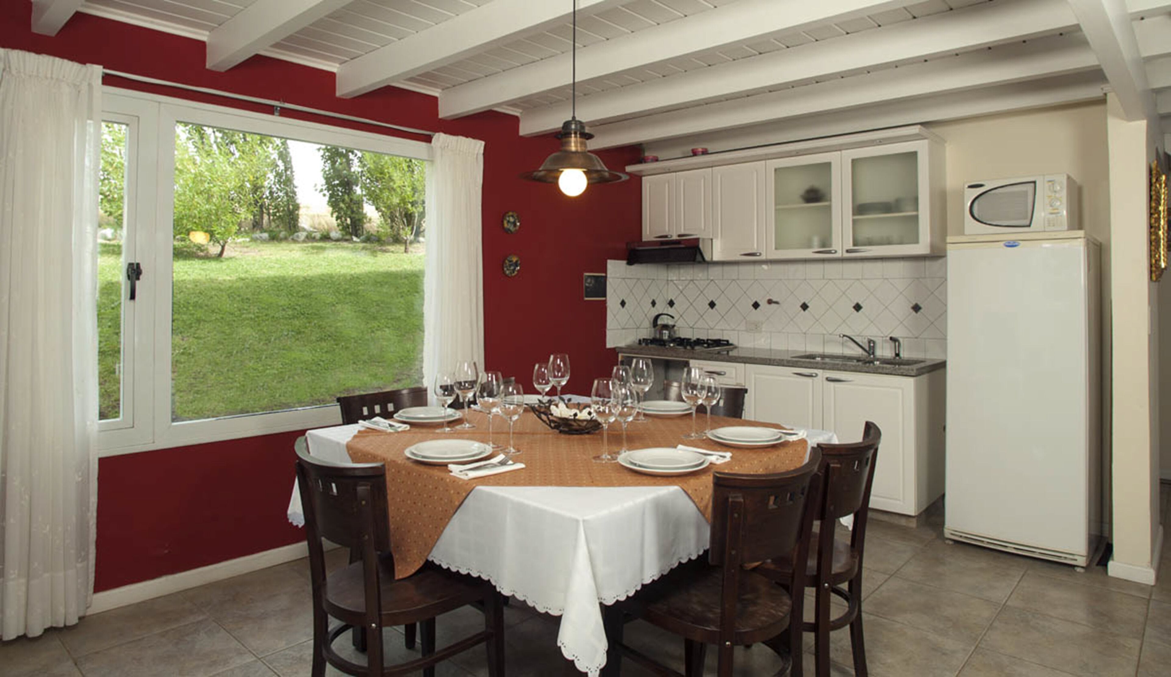 A dining area with a table set for six, surrounded by wooden chairs. There is a kitchen area with white cabinets and a microwave.