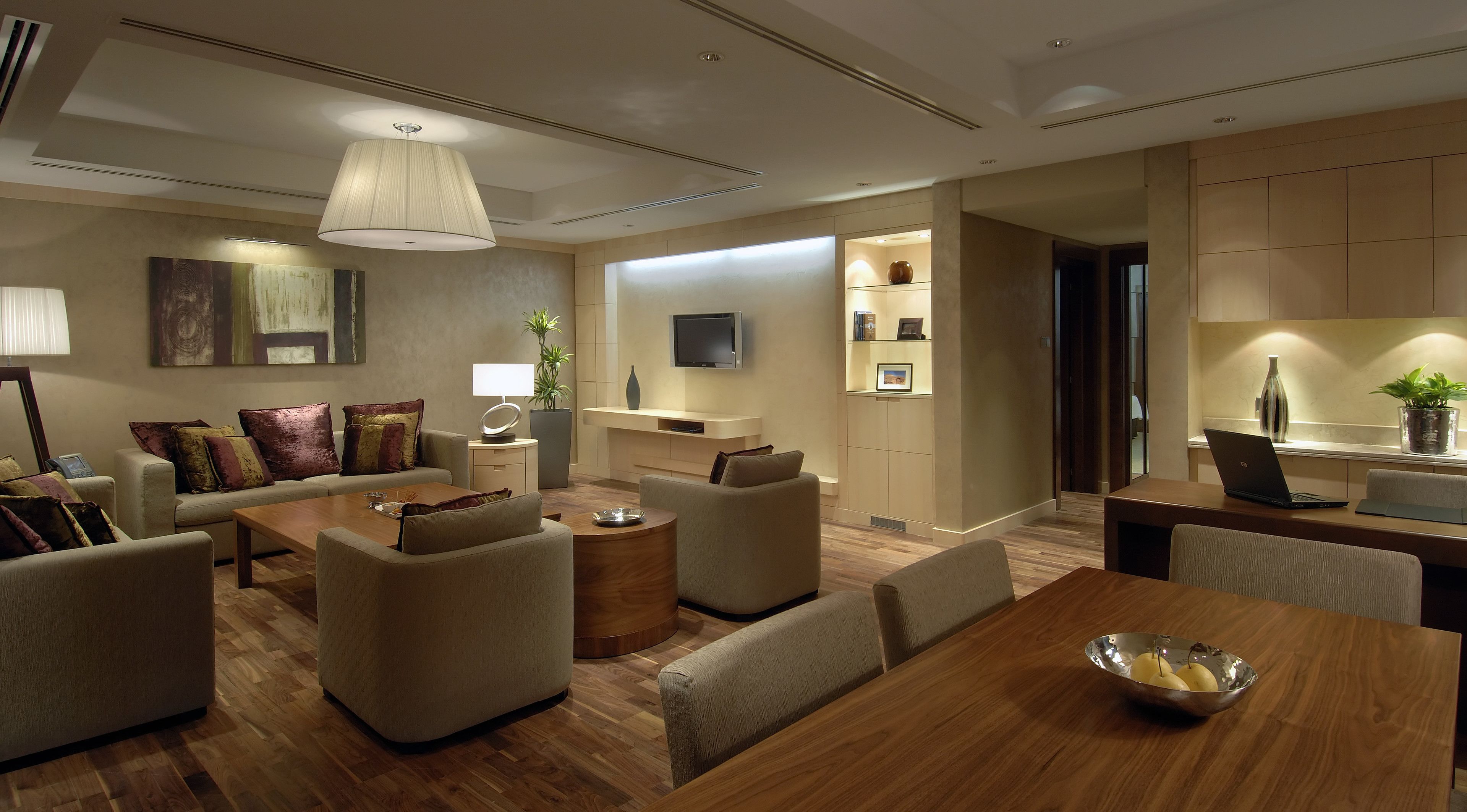 A modern living room with a sofa set, a coffee table, and a dining table with a laptop and a bowl of fruit.