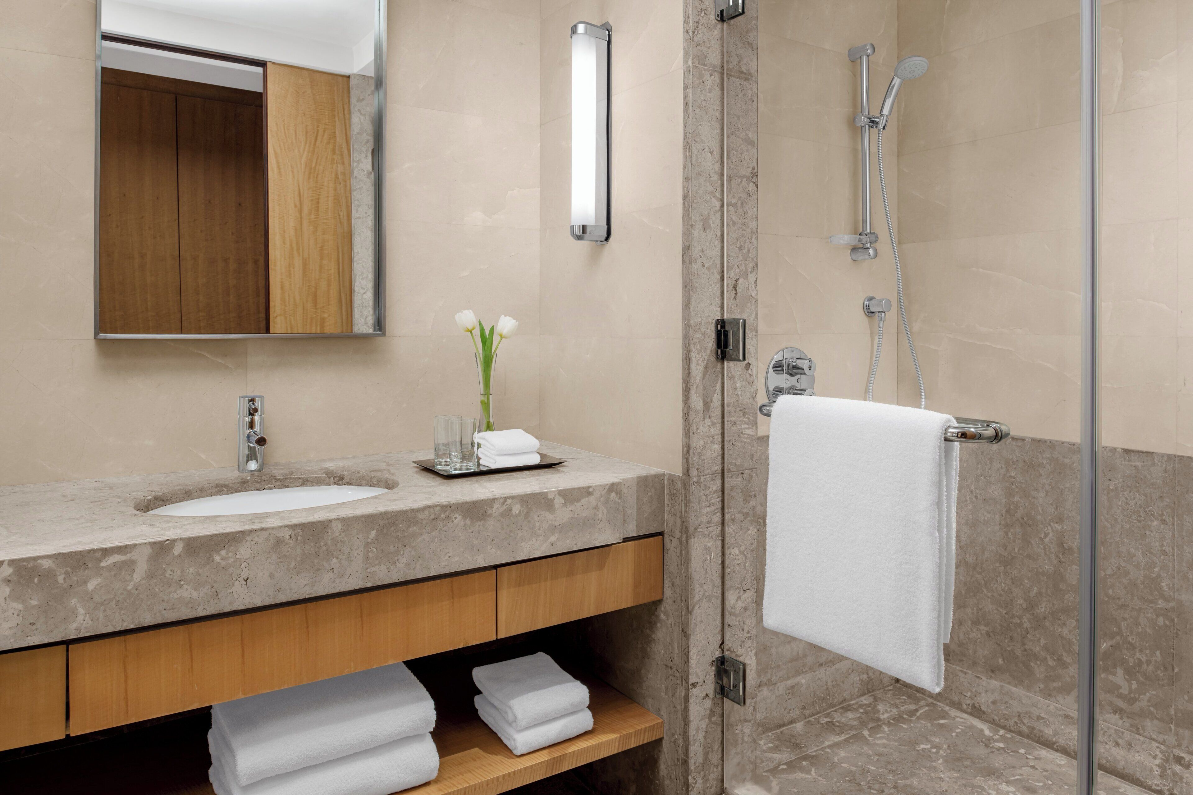 A modern bathroom with a marble sink, a glass shower enclosure, and a wooden vanity.