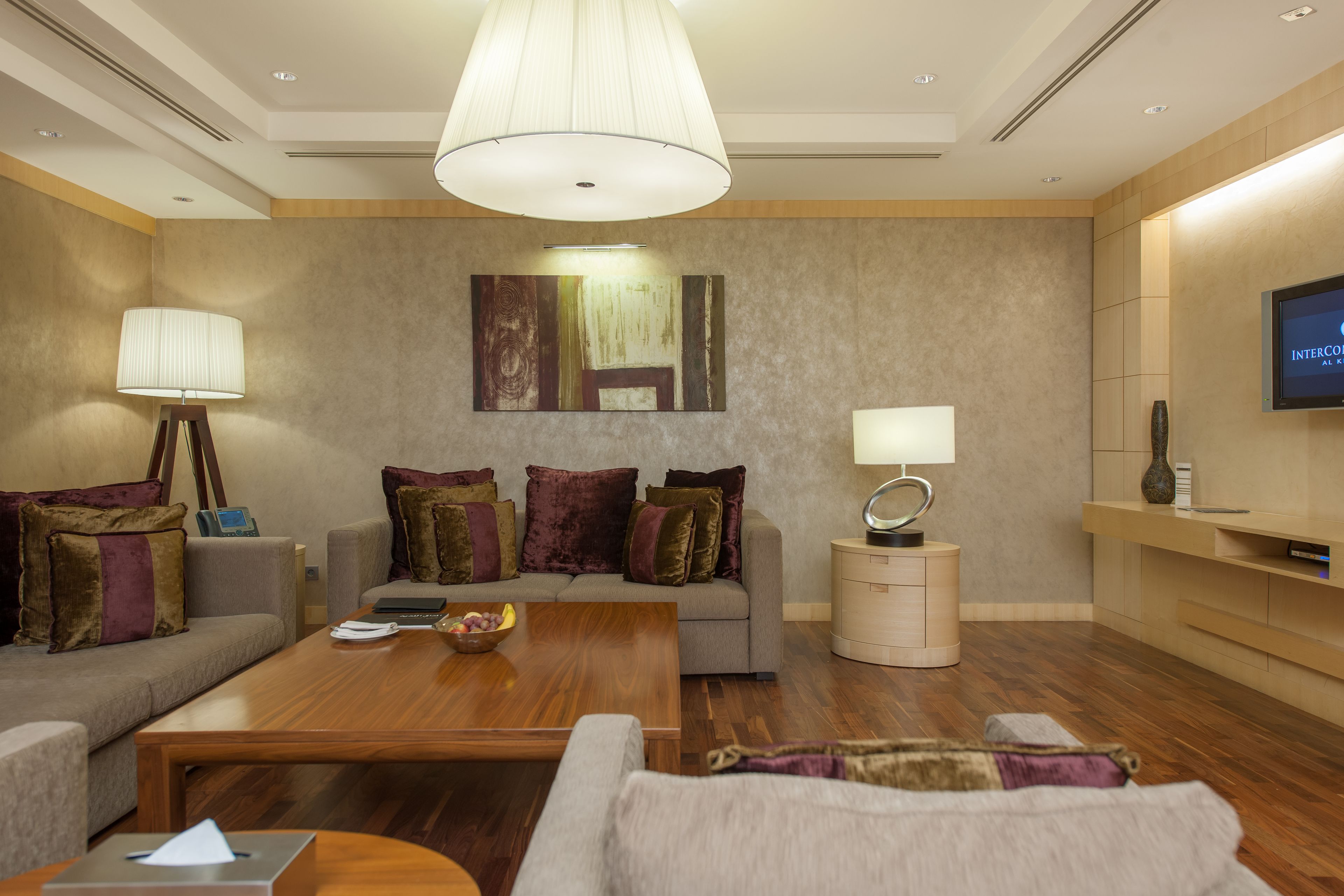 A modern hotel room with a sofa set, a wooden coffee table, a TV, and a lamp.