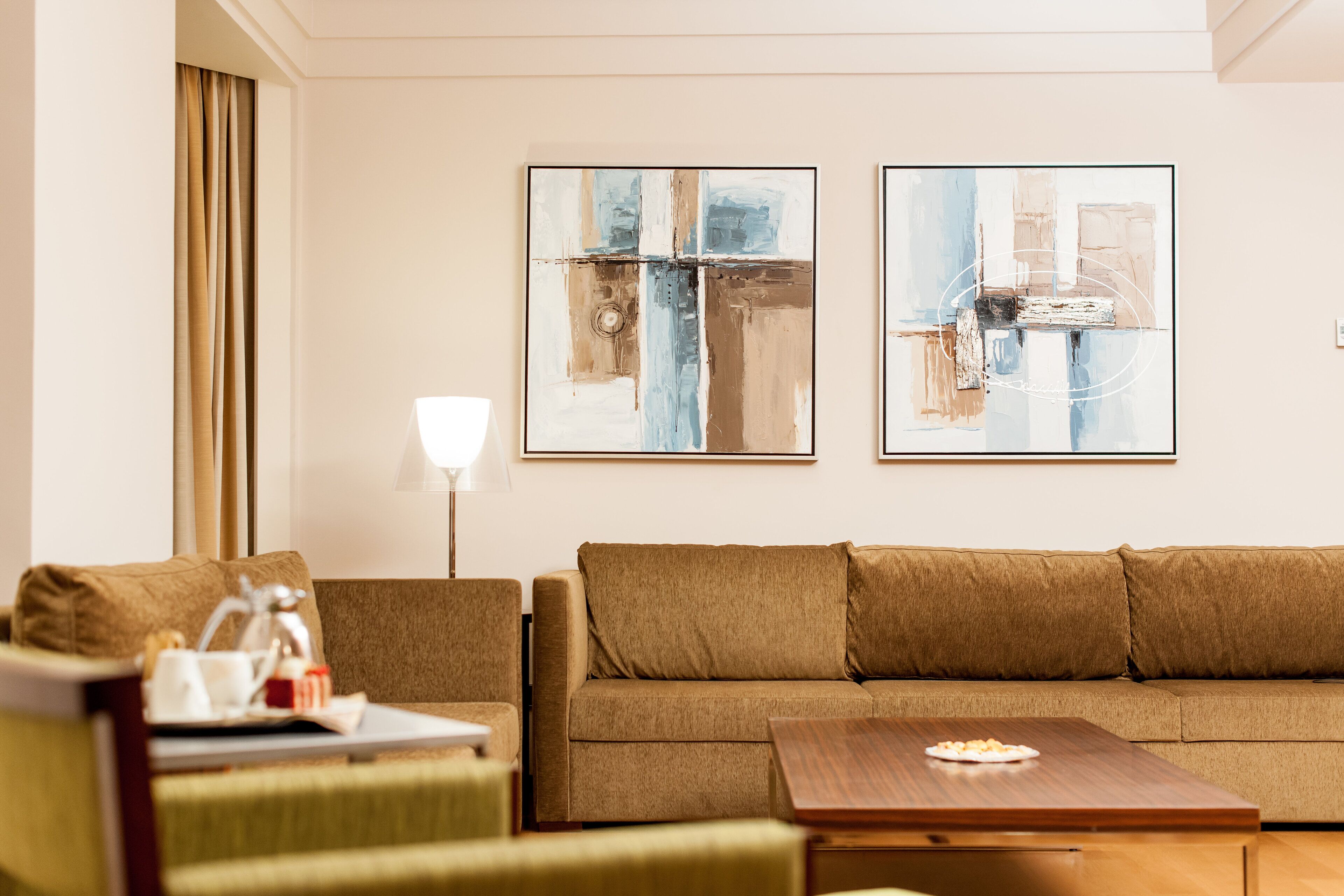 A modern living room with a sofa, a coffee table, and two abstract paintings on the wall.
