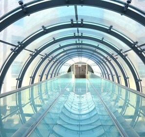 A glass-walled escalator leading to a central area with a reflective ceiling.