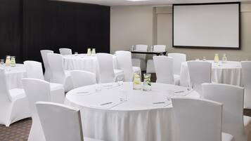 A conference room with multiple round tables, white chairs, and a projector screen.