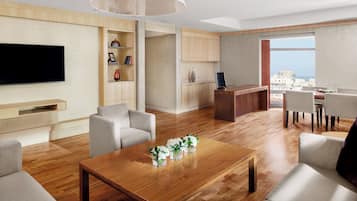 A modern living room with a flat-screen TV, a wooden coffee table with vases, and a dining area with chairs.