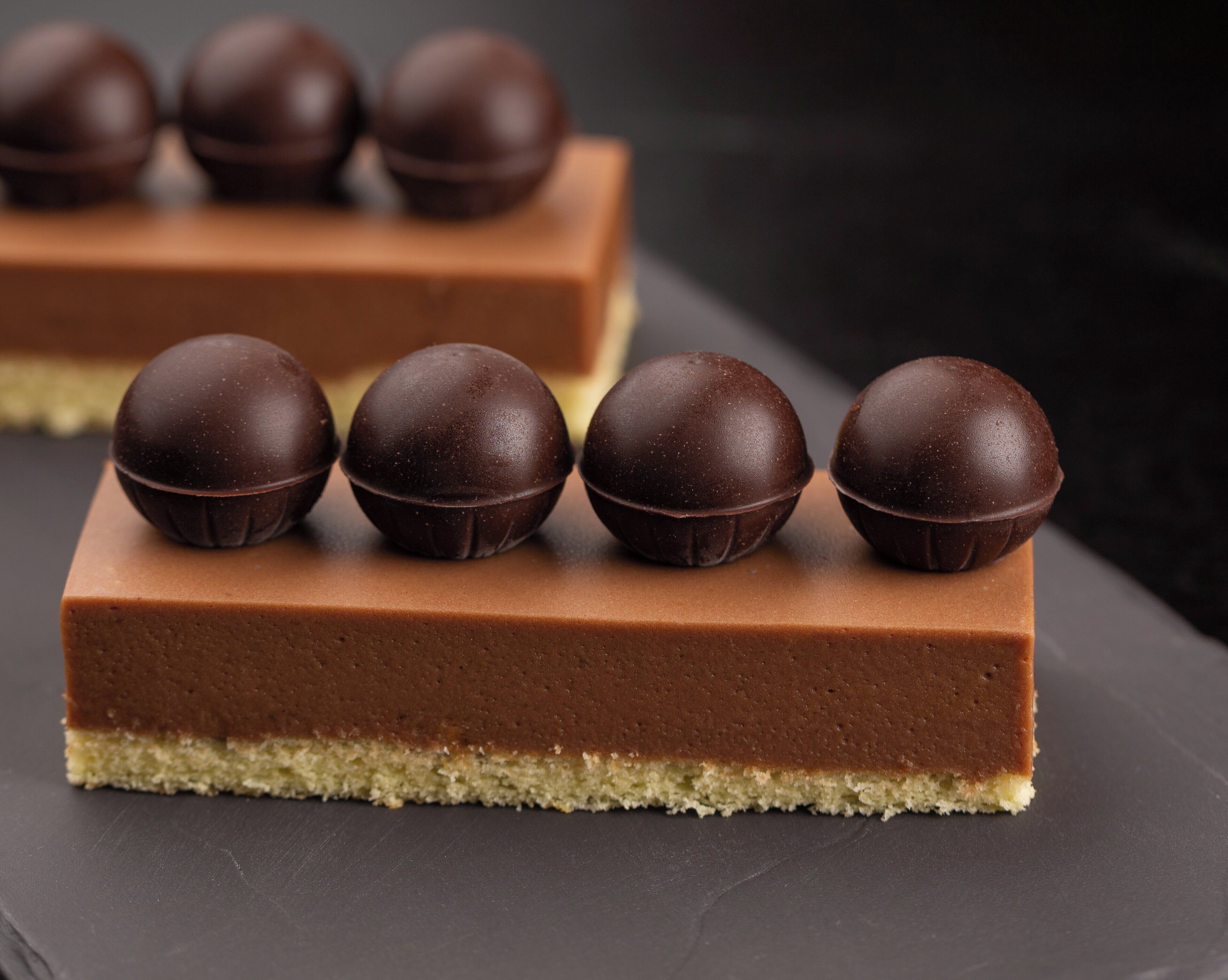 A dessert with a smooth chocolate layer and a crumbly base, topped with five chocolate balls.