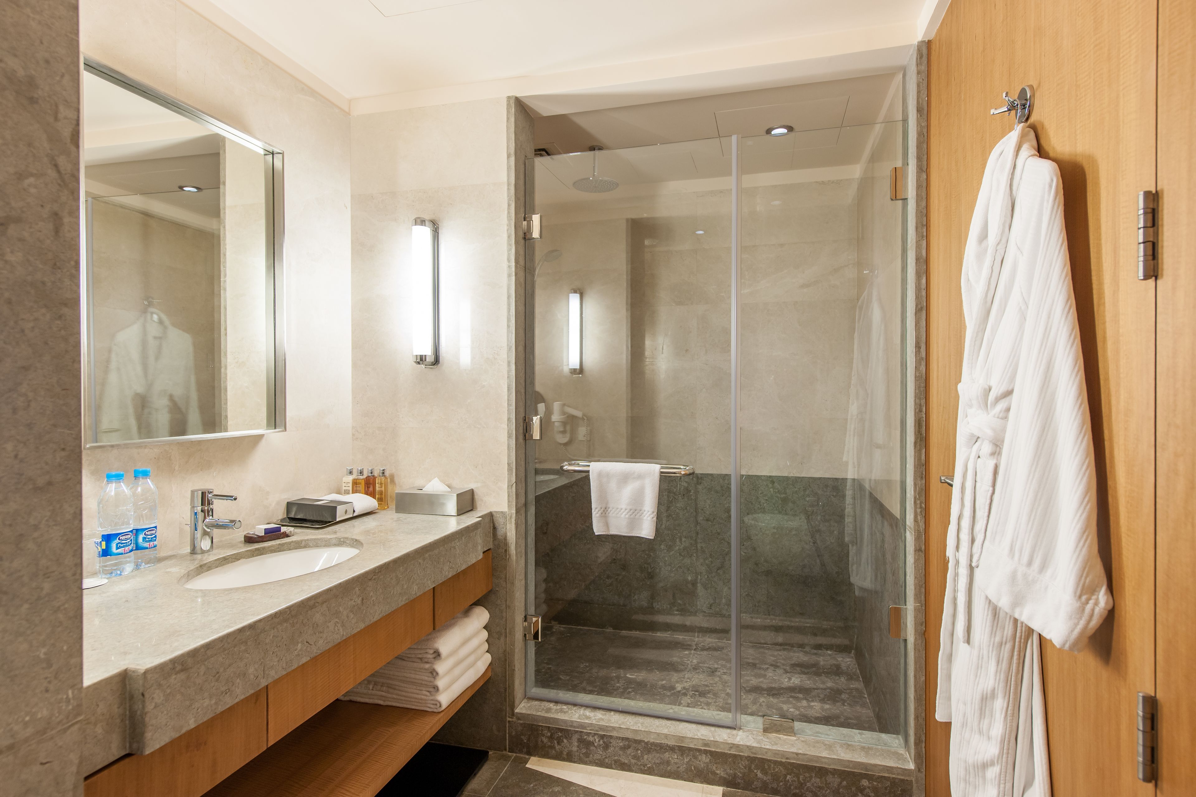 A modern bathroom with a glass-enclosed shower, a large mirror, and a wooden vanity with a sink and towel rack.