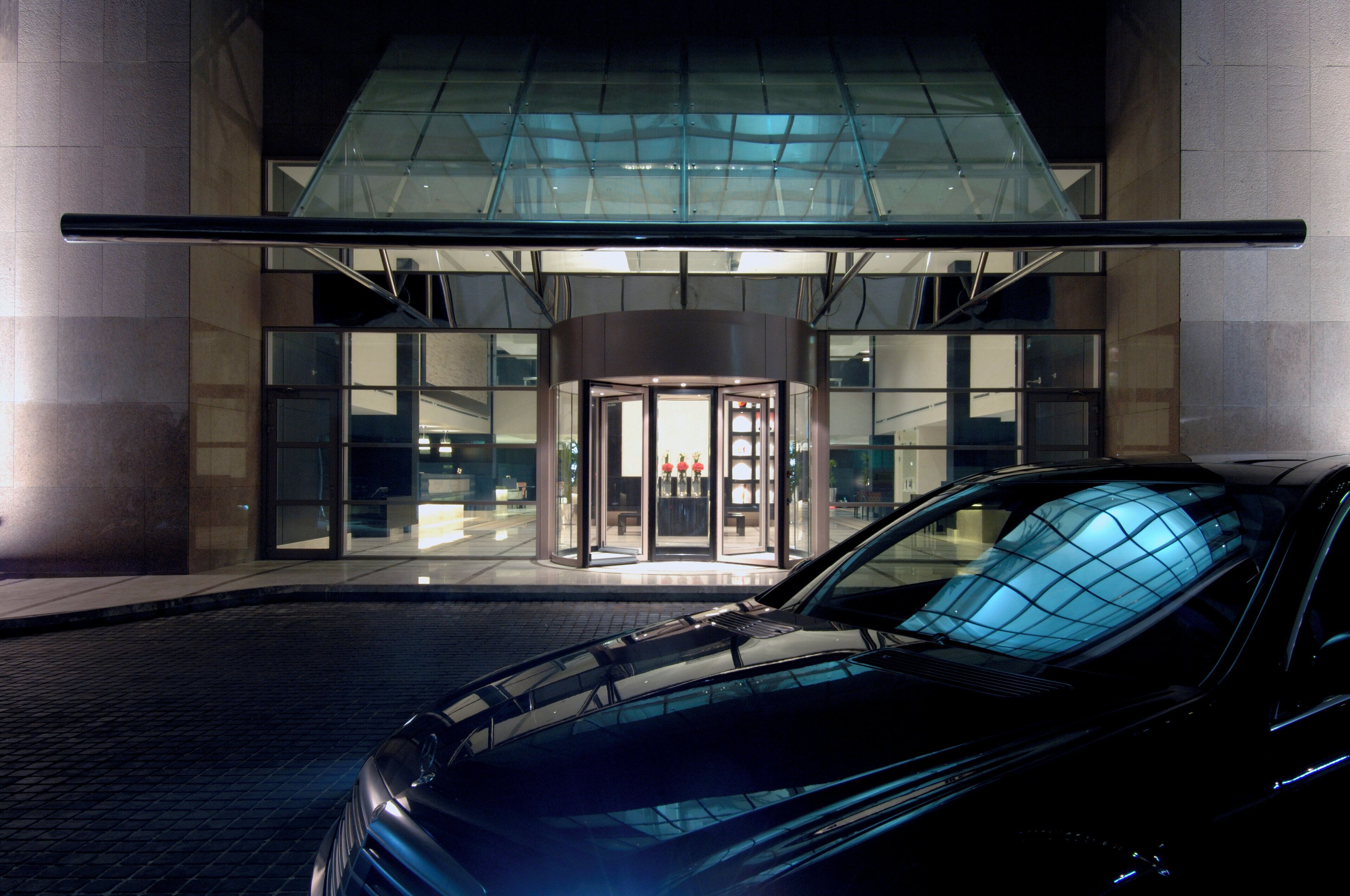 Un edificio moderno con entrada de vidrio y un coche estacionado adelante.