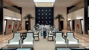 A modern hotel lobby with a central reception desk, two palm trees, and a patterned carpet.