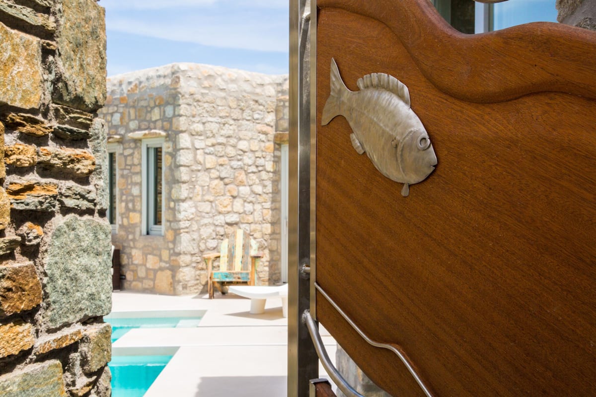 A stone building with a pool, wooden door with a fish carving, and a view of the pool area.