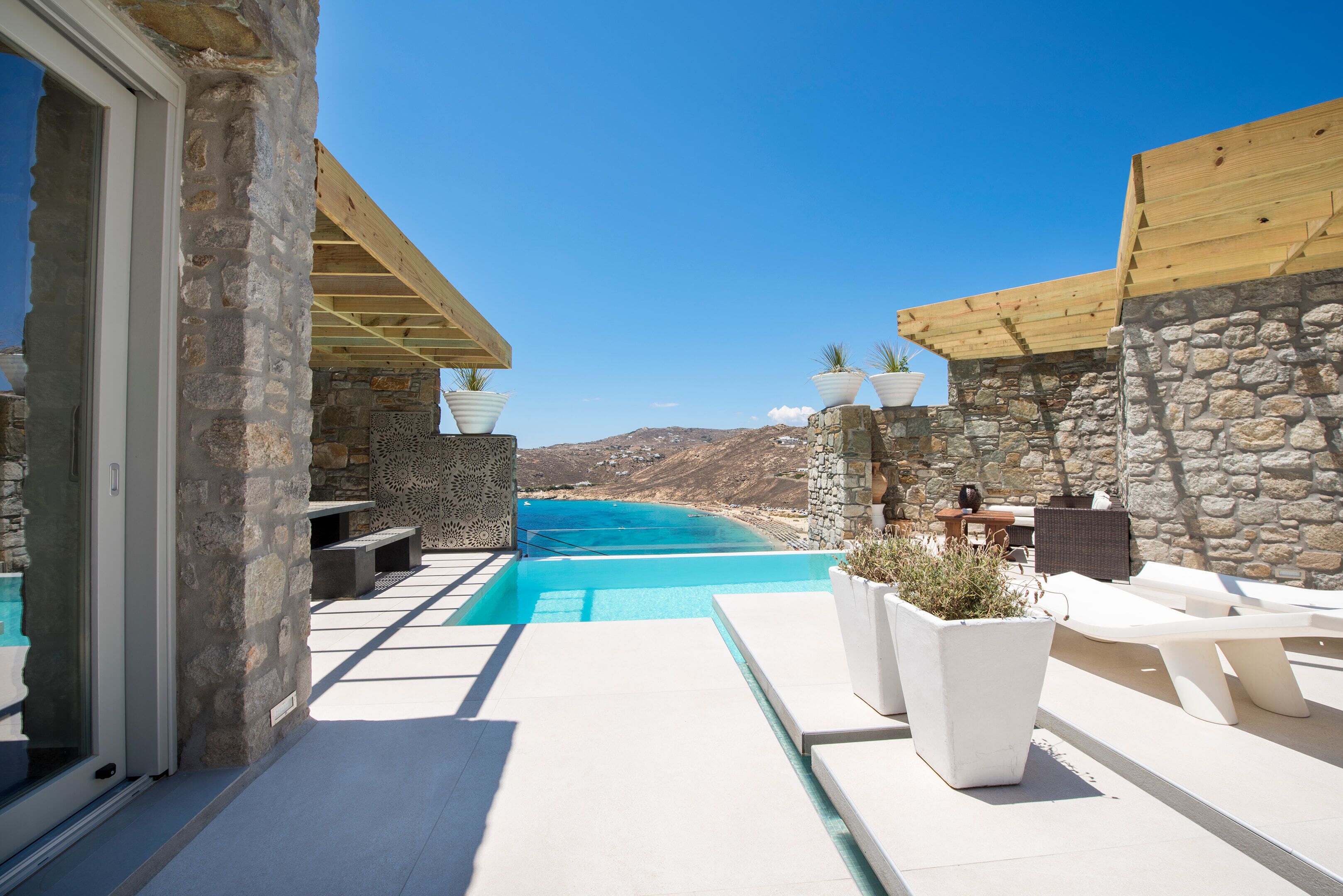 A pool area with stone walls, wooden pergolas, and outdoor seating.