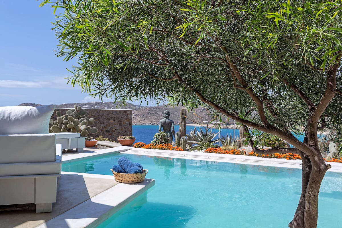A pool area with a white lounge chair, a basket with towels, and a statue.