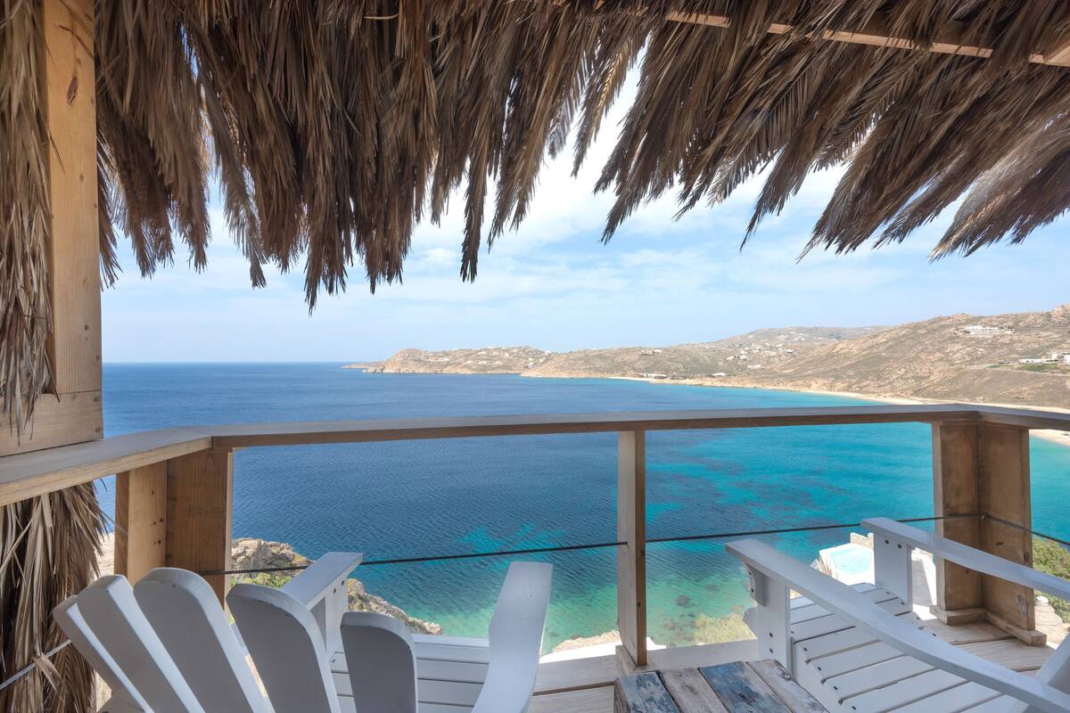 A wooden deck with white chairs overlooking a coastal view.