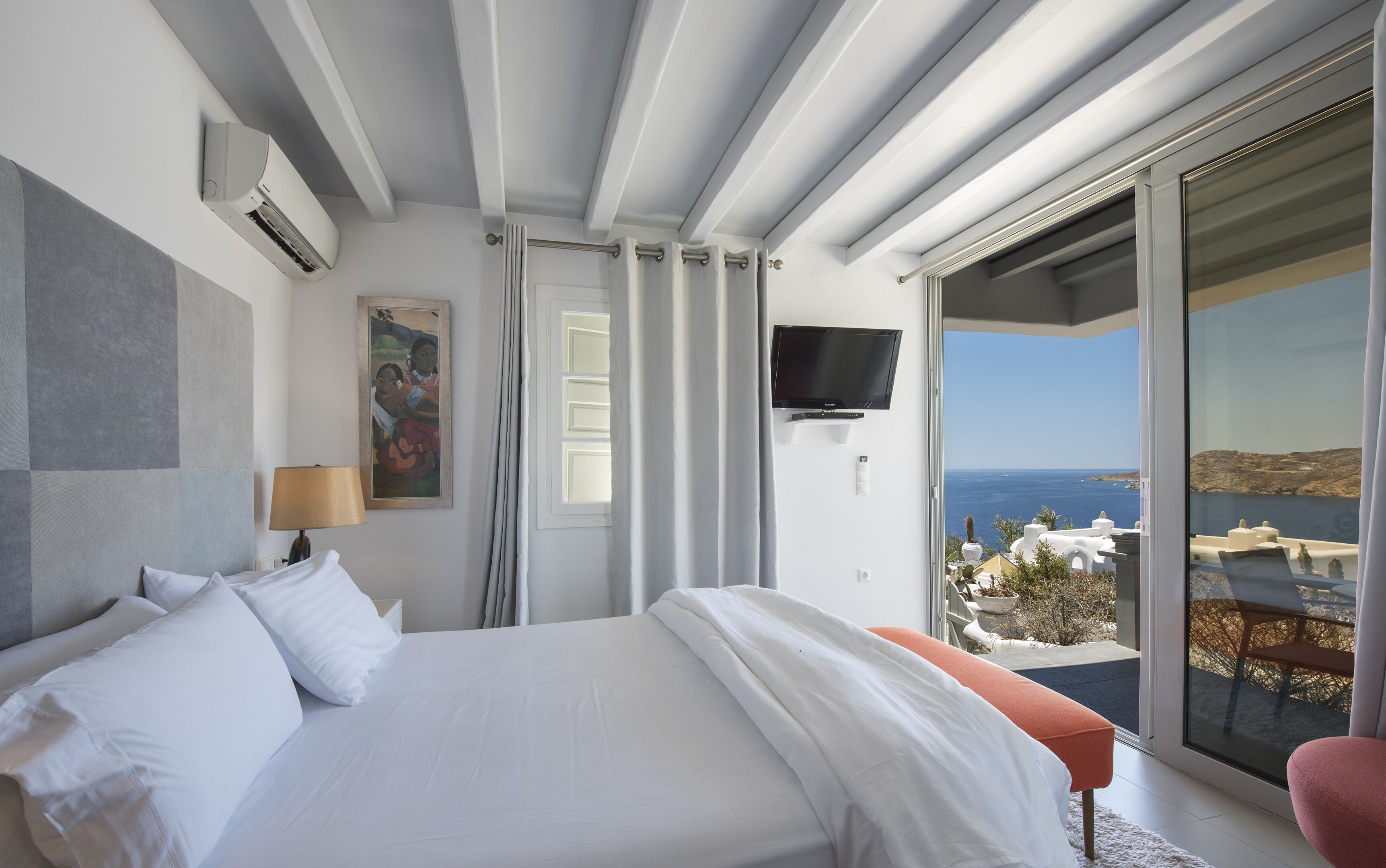A bedroom with a bed, a TV, a painting, and a balcony with a view.