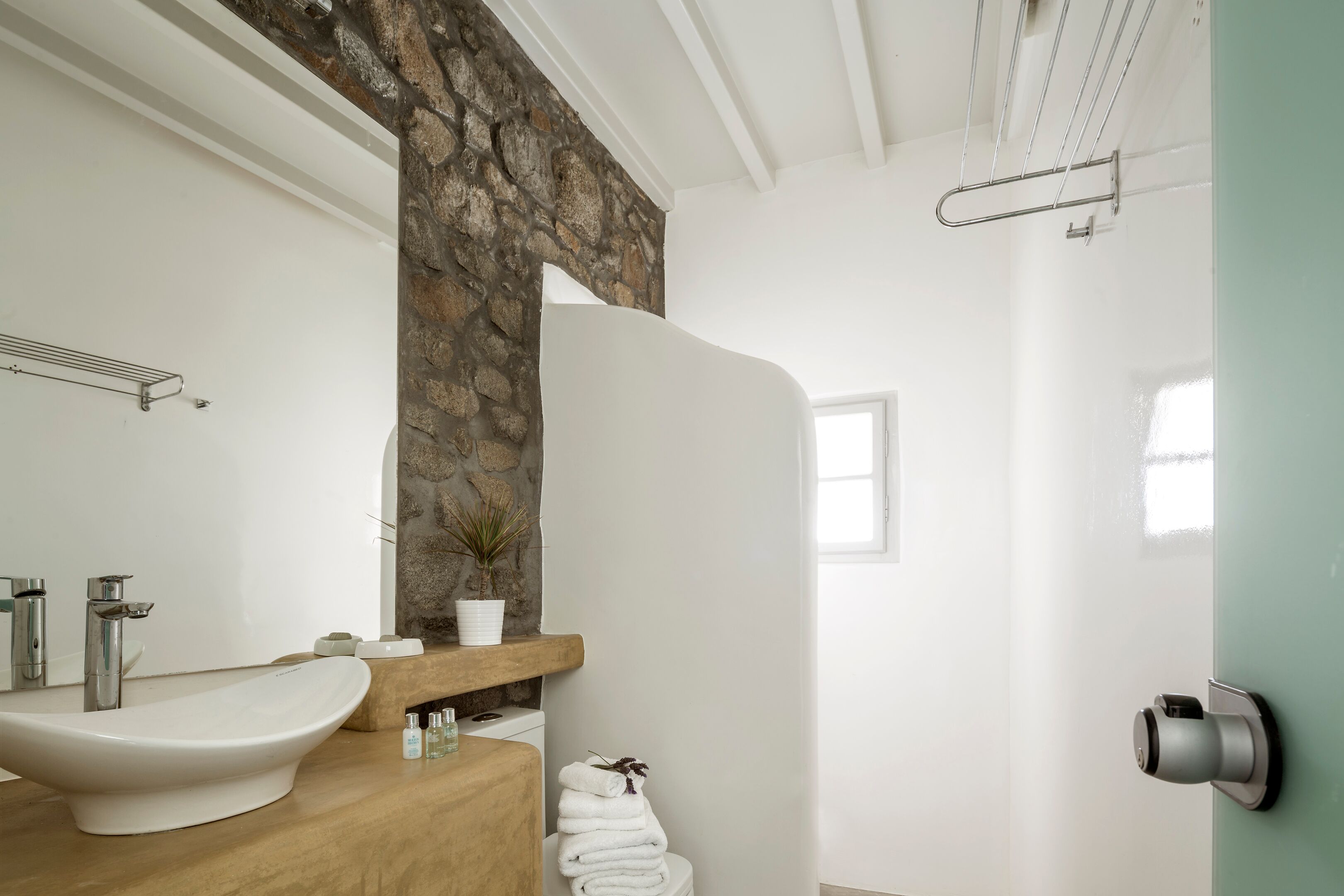 A bathroom with a stone accent wall, a white sink, a towel rack, and a shower door.