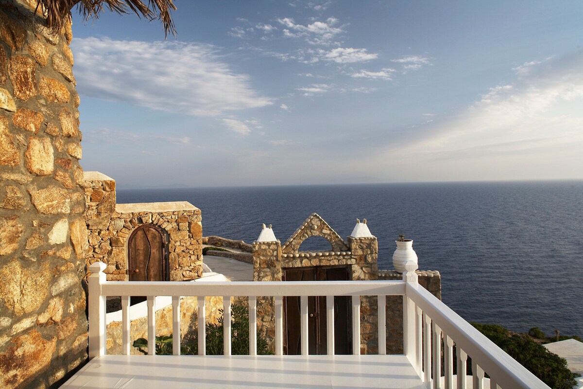 A stone building with a white balcony railing overlooking the sea.