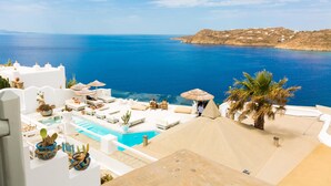 A resort with a pool, sun loungers, umbrellas, and a view of the sea. - Greco Philia Hotel Boutique by Mr and Mrs White (Mykonos)
