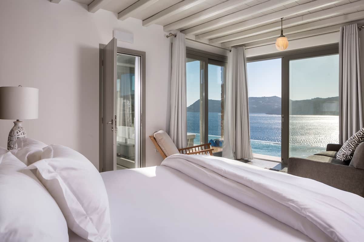 A hotel room with a bed, a chair, a lamp, and a view of the sea.