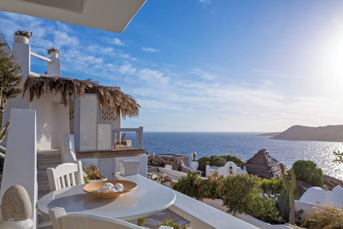 A white outdoor seating area with a table and chairs, overlooking the sea.