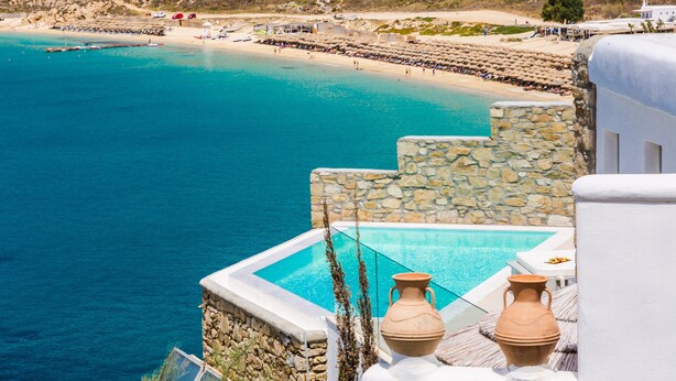 A coastal hotel with a pool, stone walls, and a view of the beach. - Greco Philia Hotel Boutique by Mr and Mrs White (Mykonos)