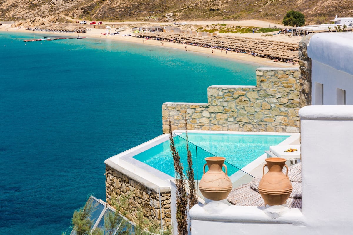 A coastal hotel with a pool, stone walls, and a view of the beach.