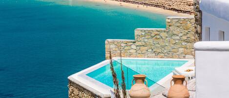 A coastal hotel with a pool, stone walls, and a view of the beach.