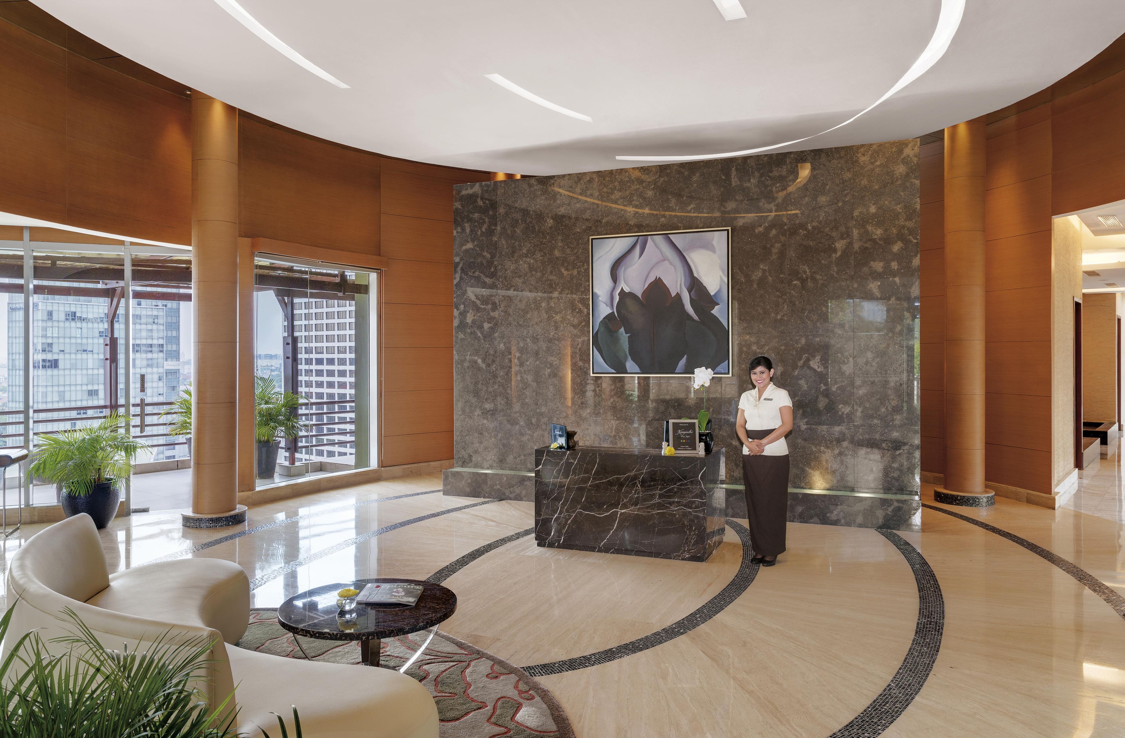 A hotel lobby with a reception desk, a large abstract painting, and a receptionist.