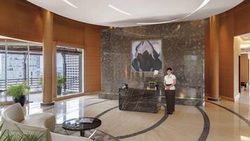 A hotel lobby with a reception desk, a large abstract painting, and a receptionist.