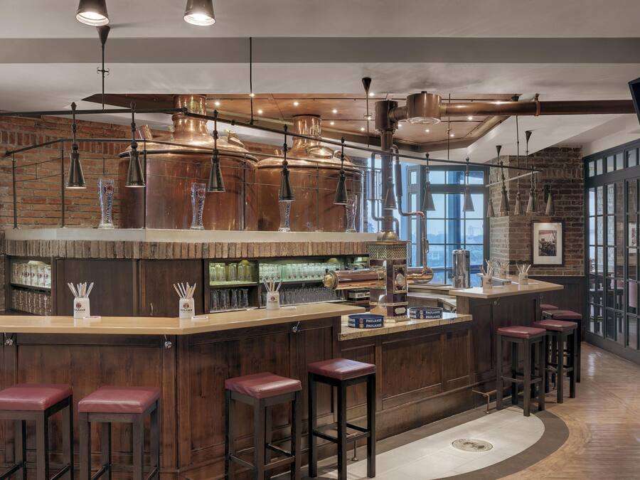 A bar area with a brick wall, copper beer taps, and wooden stools.