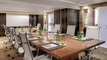 A conference room with a long wooden table, white chairs, and a whiteboard.
