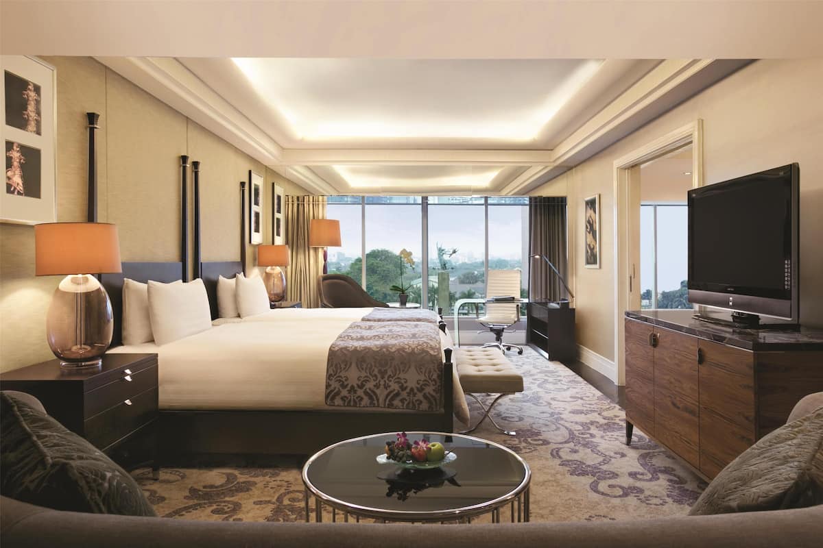 A hotel room with a large bed, a television, a desk with a lamp, and a view of the city.