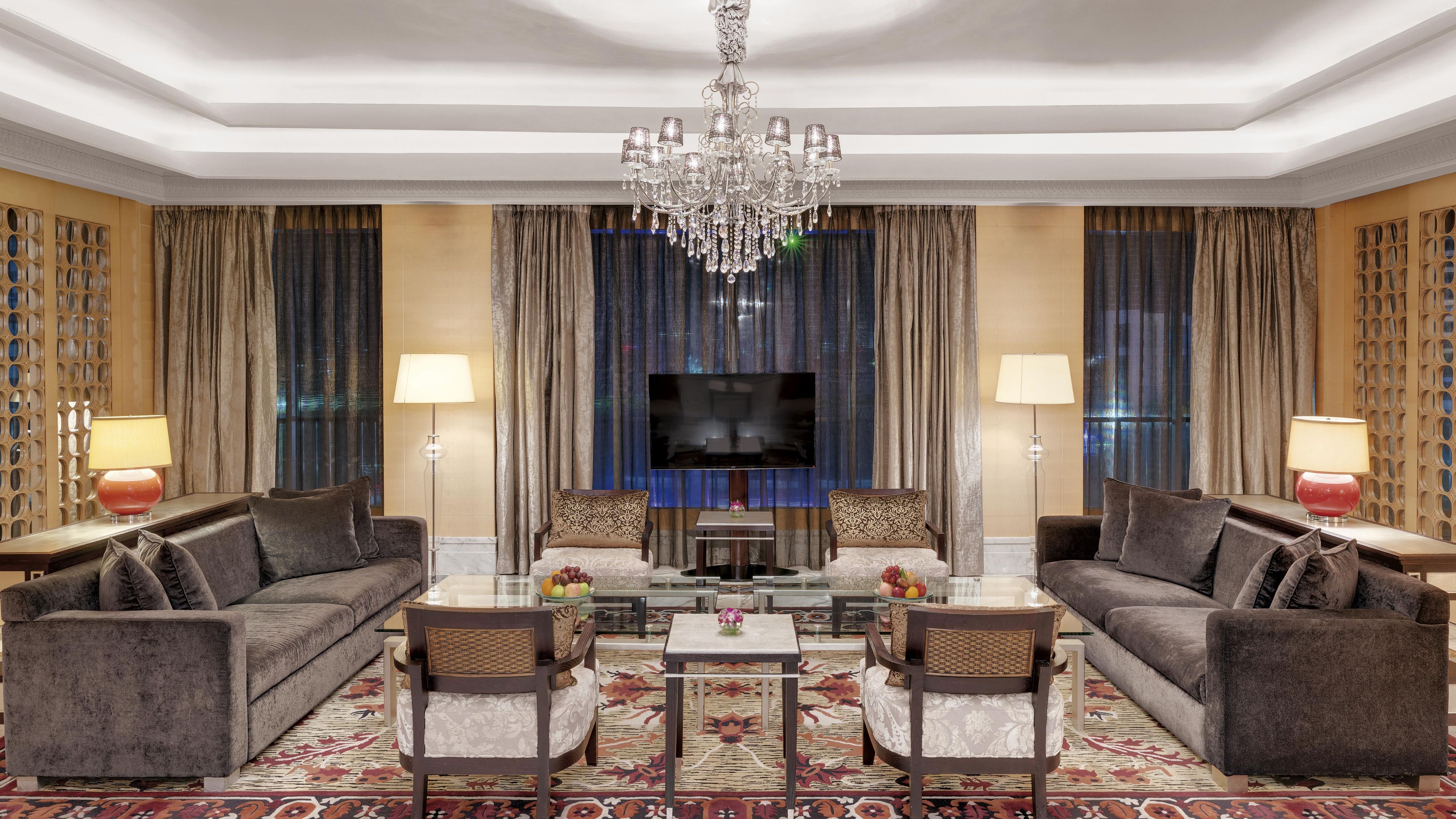 A spacious living room with a large flat-screen TV, two sofas, a coffee table, and a chandelier.