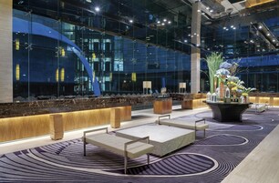A modern lobby with a reception desk, seating areas, and a large glass wall reflecting the building's interior.