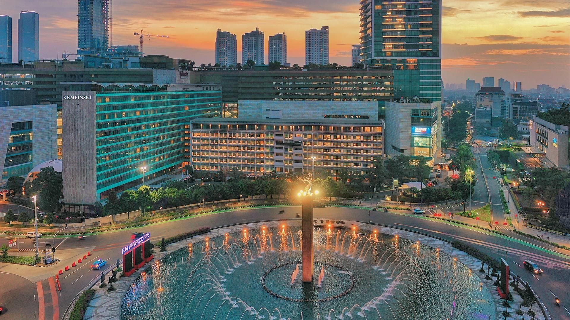 A cityscape with a prominent building featuring a large fountain in the center.