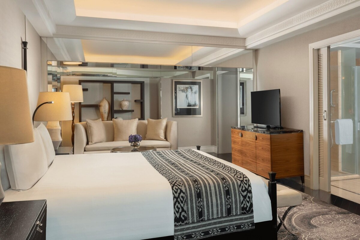 Une chambre d’hôtel avec un grand lit, une télévision, une commode en bois et une douche fermée par des parois de verre.