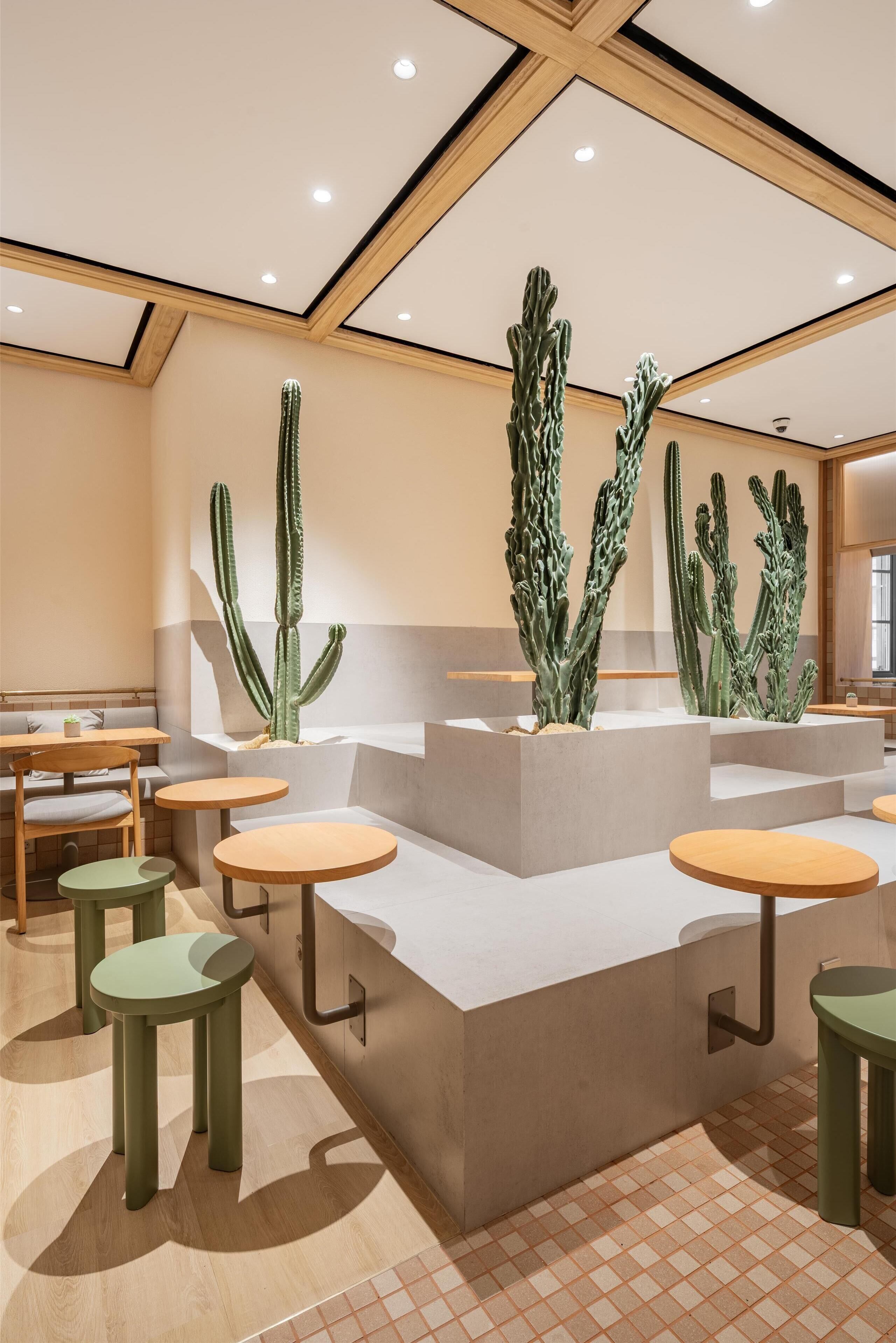 A modern interior with a central seating area featuring round tables and chairs, surrounded by large cacti sculptures.
