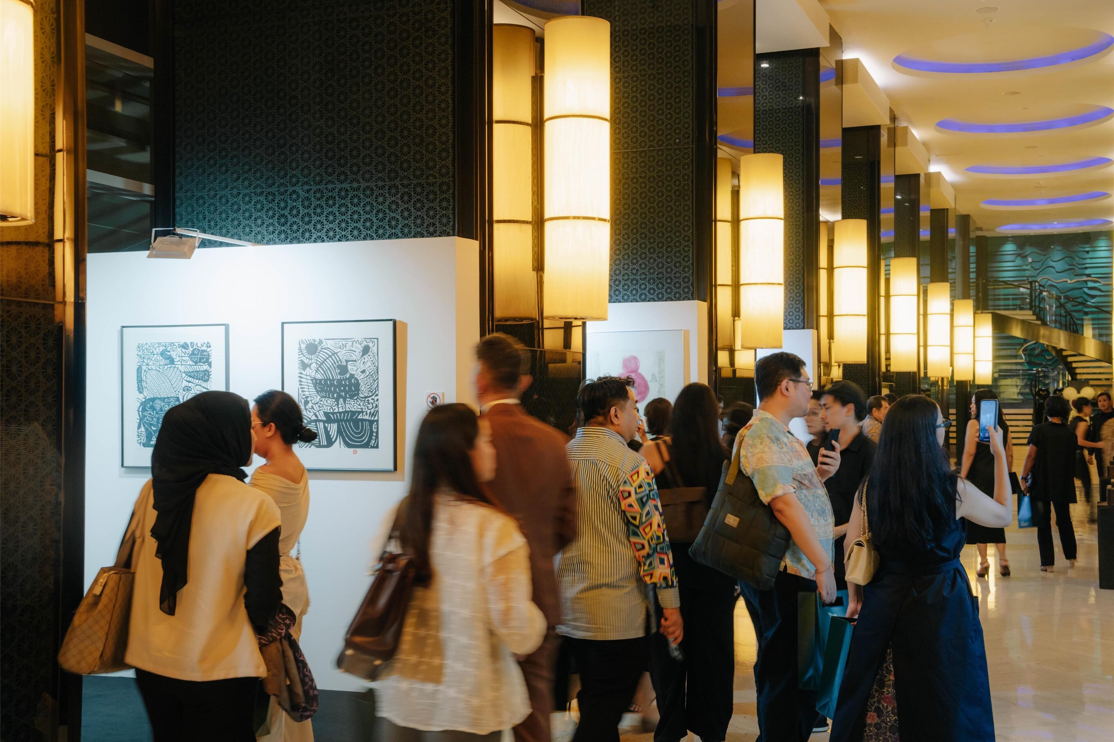 A hotel lobby with a modern design, featuring a staircase, artwork on the walls, and a crowd of people.