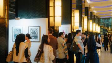 A hotel lobby with a modern design, featuring a staircase, artwork on the walls, and a crowd of people.