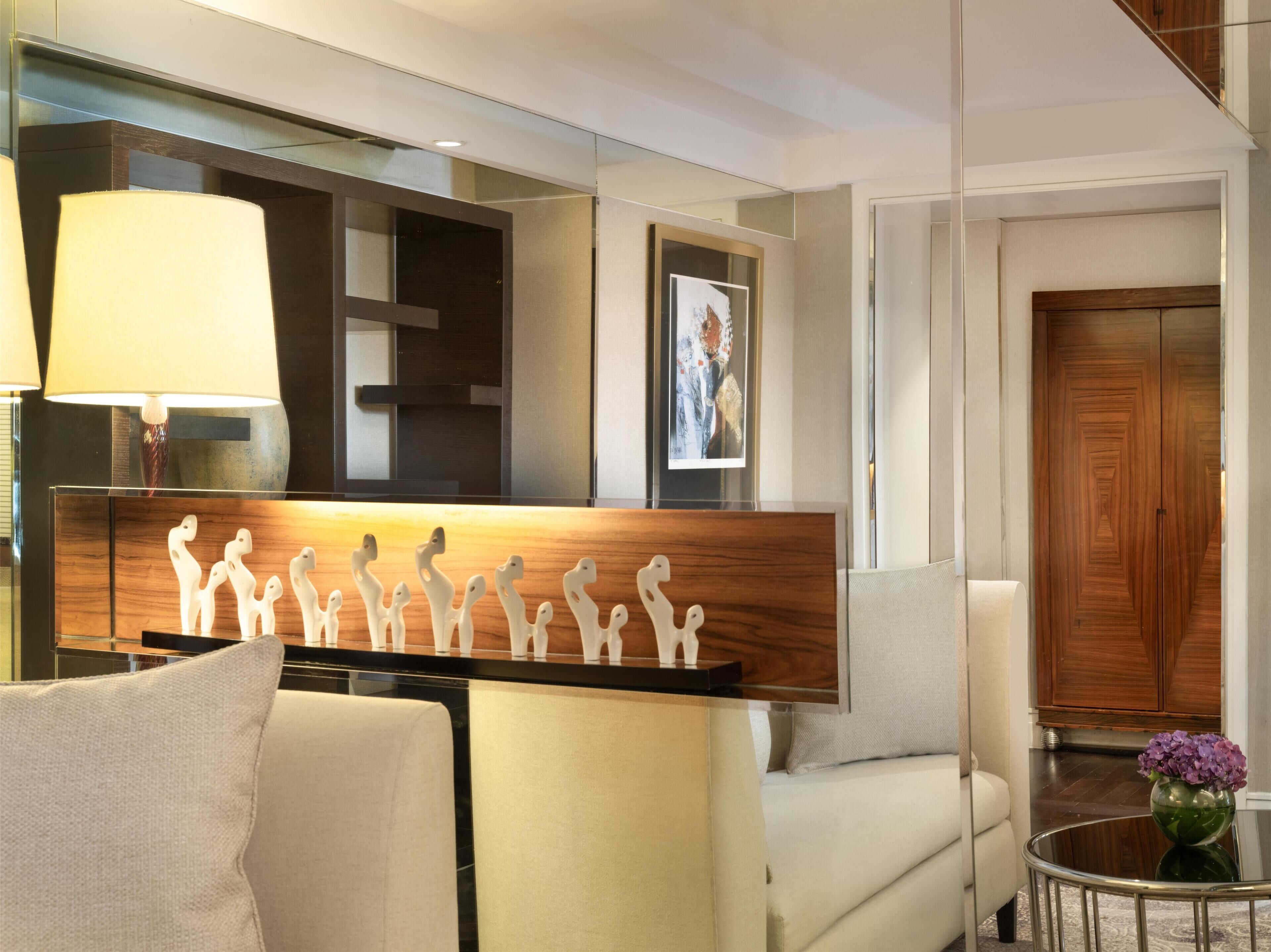 A modern hotel room with a sofa, a side table with a vase, a lamp, a wooden headboard, and a framed picture on the wall.