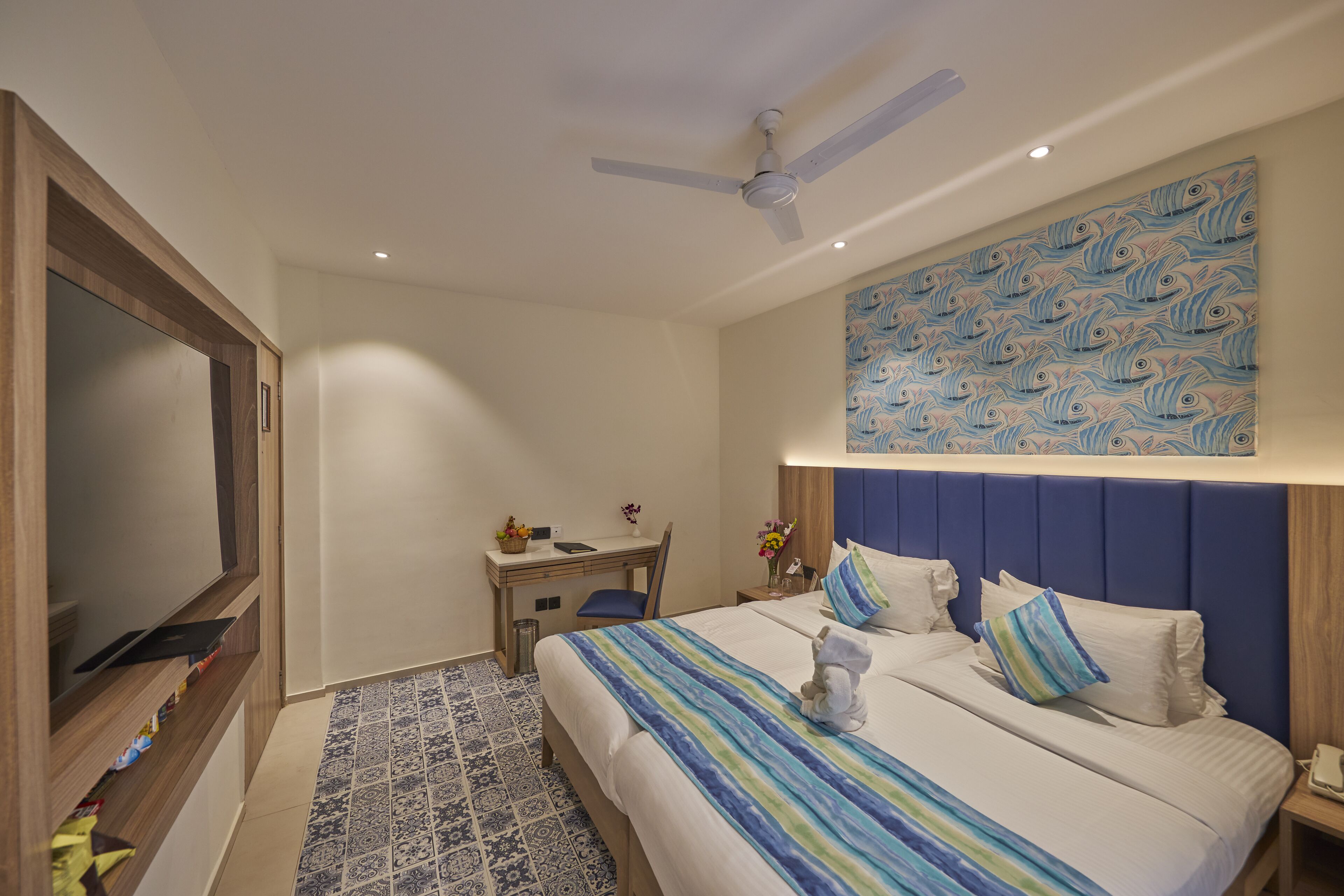 Habitación de hotel con cama, escritorio, silla, televisor y ventilador de techo.