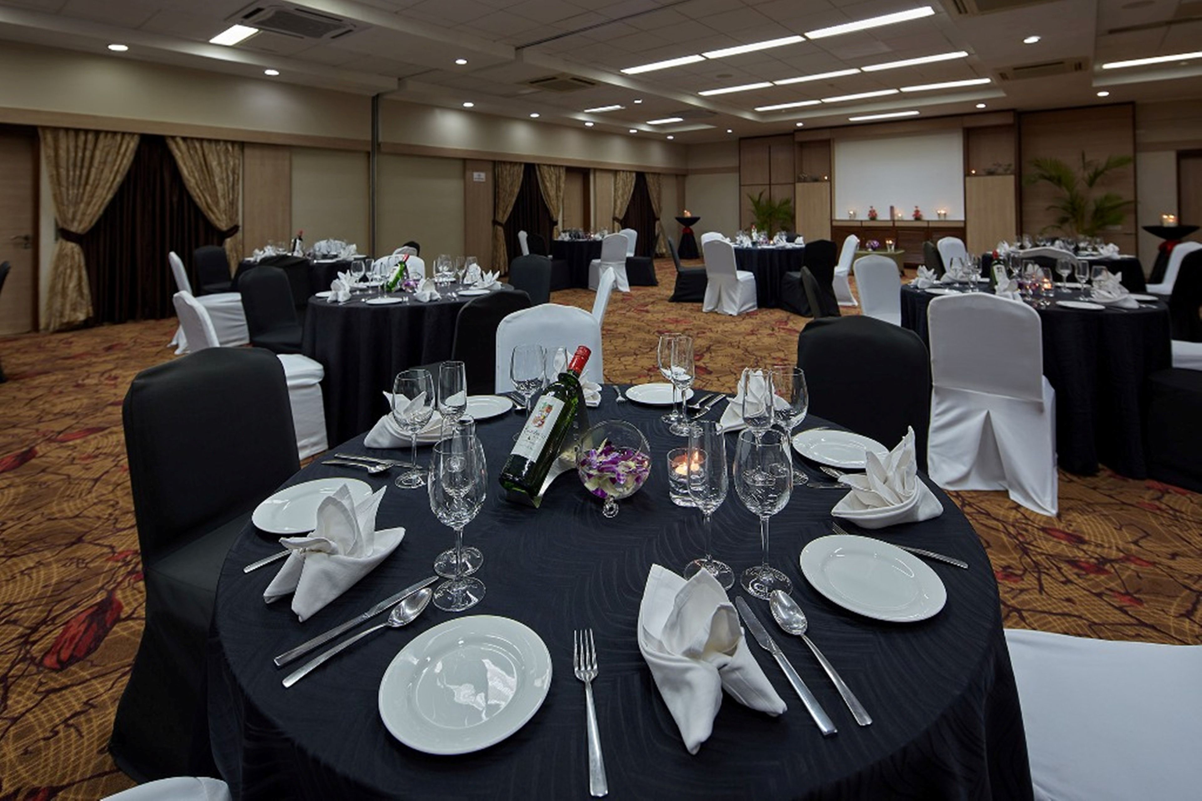 A banquet hall with round tables set for dining, featuring white tablecloths, silverware, and wine glasses.
