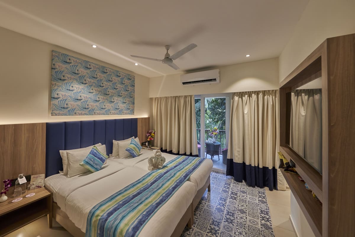 A modern hotel room with a large bed, a ceiling fan, an air conditioning unit, a large window with curtains, and a decorative wall piece.
