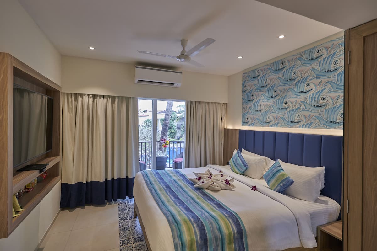 A hotel room with a bed, a TV, a ceiling fan, and a view of the outdoors.
