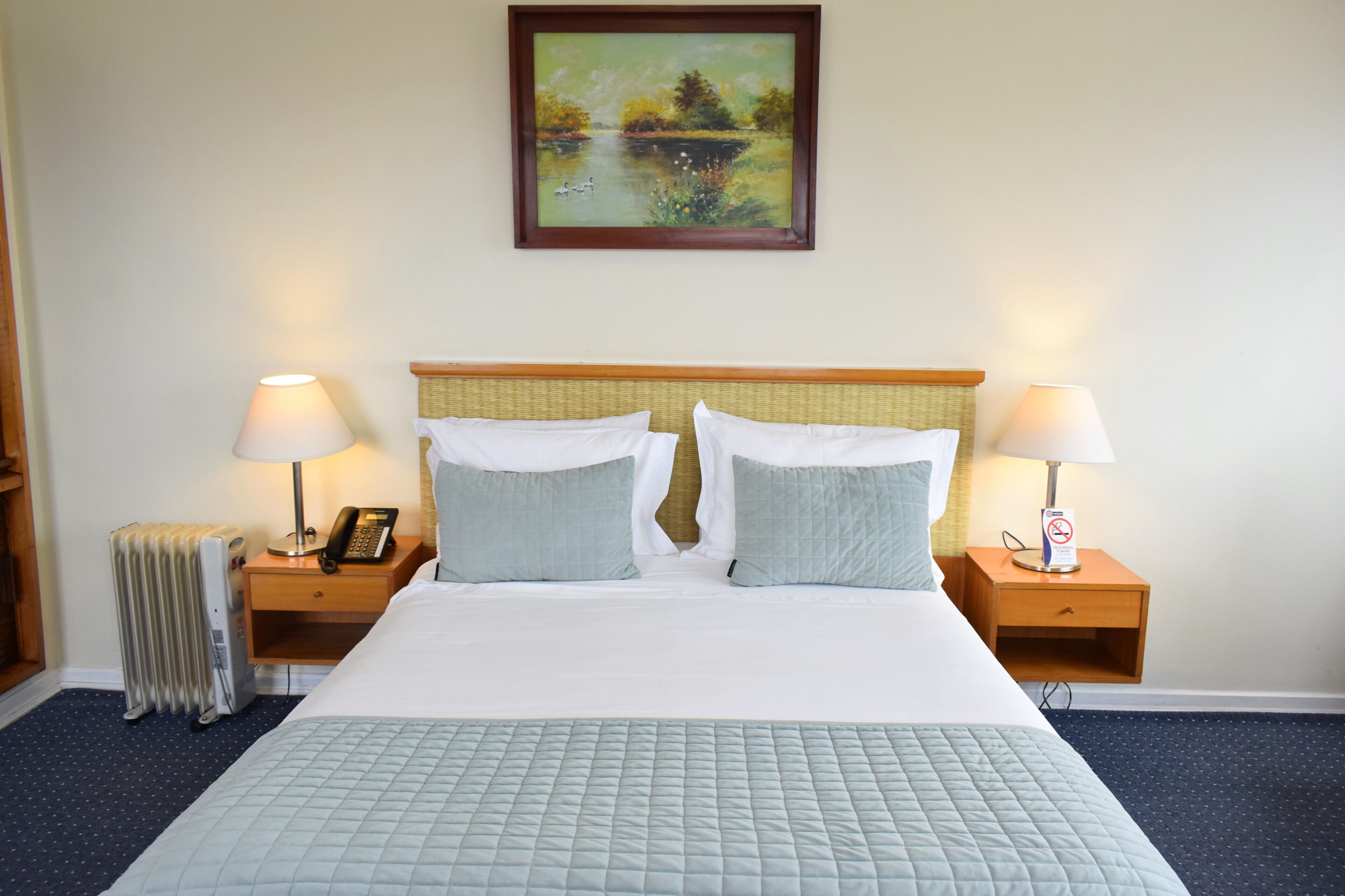 A hotel room with a large bed, two bedside tables with lamps, a painting on the wall, and a radiator.