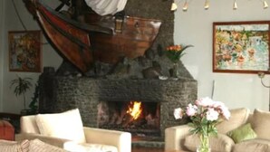 A cozy living room with a fireplace, comfortable seating, and decorative elements like a hanging light fixture and artwork. - Gran Hotel Vicente Costanera (Puerto Montt)