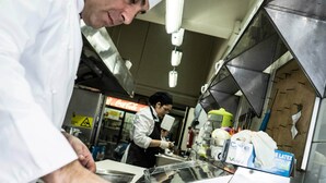 A chef preparing food in a professional kitchen with stainless steel surfaces and various kitchen equipment. - Gran Hotel Vicente Costanera (Puerto Montt)