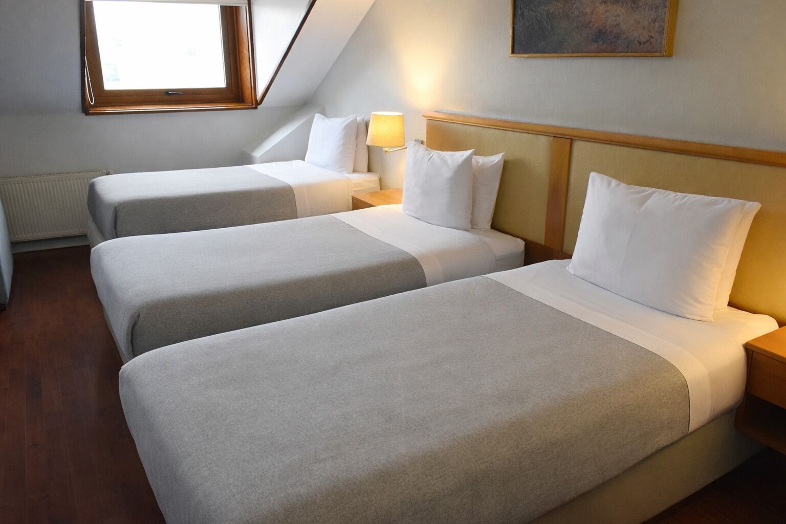 Une chambre d’hôtel avec deux lits, une fenêtre, un radiateur et un tableau au mur.