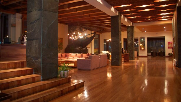 A spacious lobby with a wooden staircase, a seating area with sofas, and a large stone pillar. - Gran Hotel Vicente Costanera (Puerto Montt)