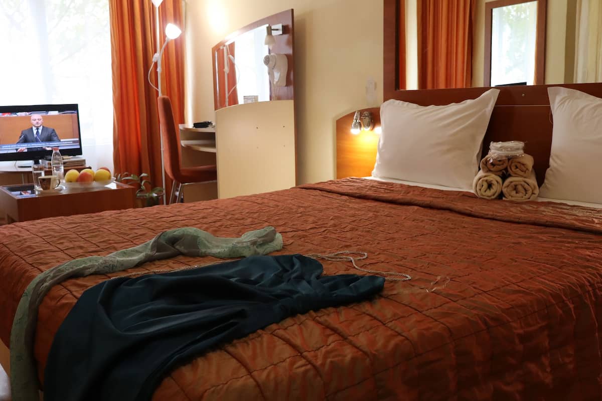 A hotel room with a bed, a TV on a desk, a lamp, and a mirror.