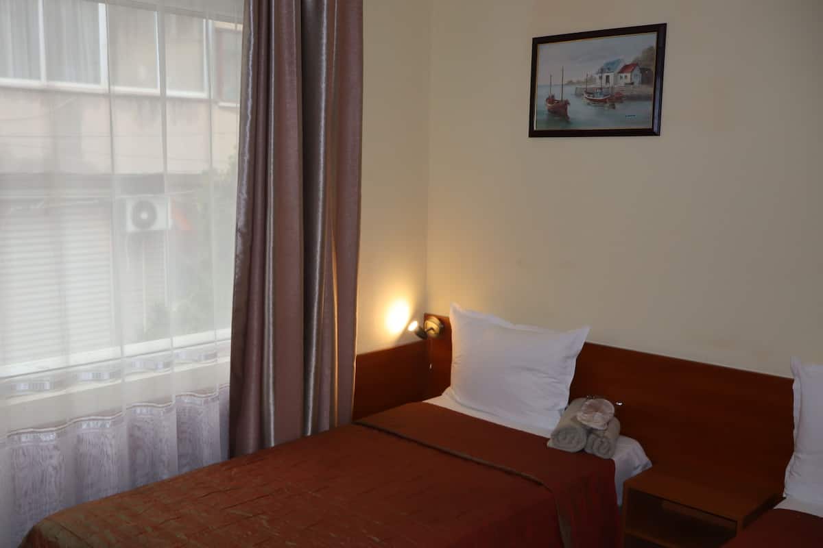 A hotel room with a bed, a nightstand, a lamp, a painting, and a window with curtains.
